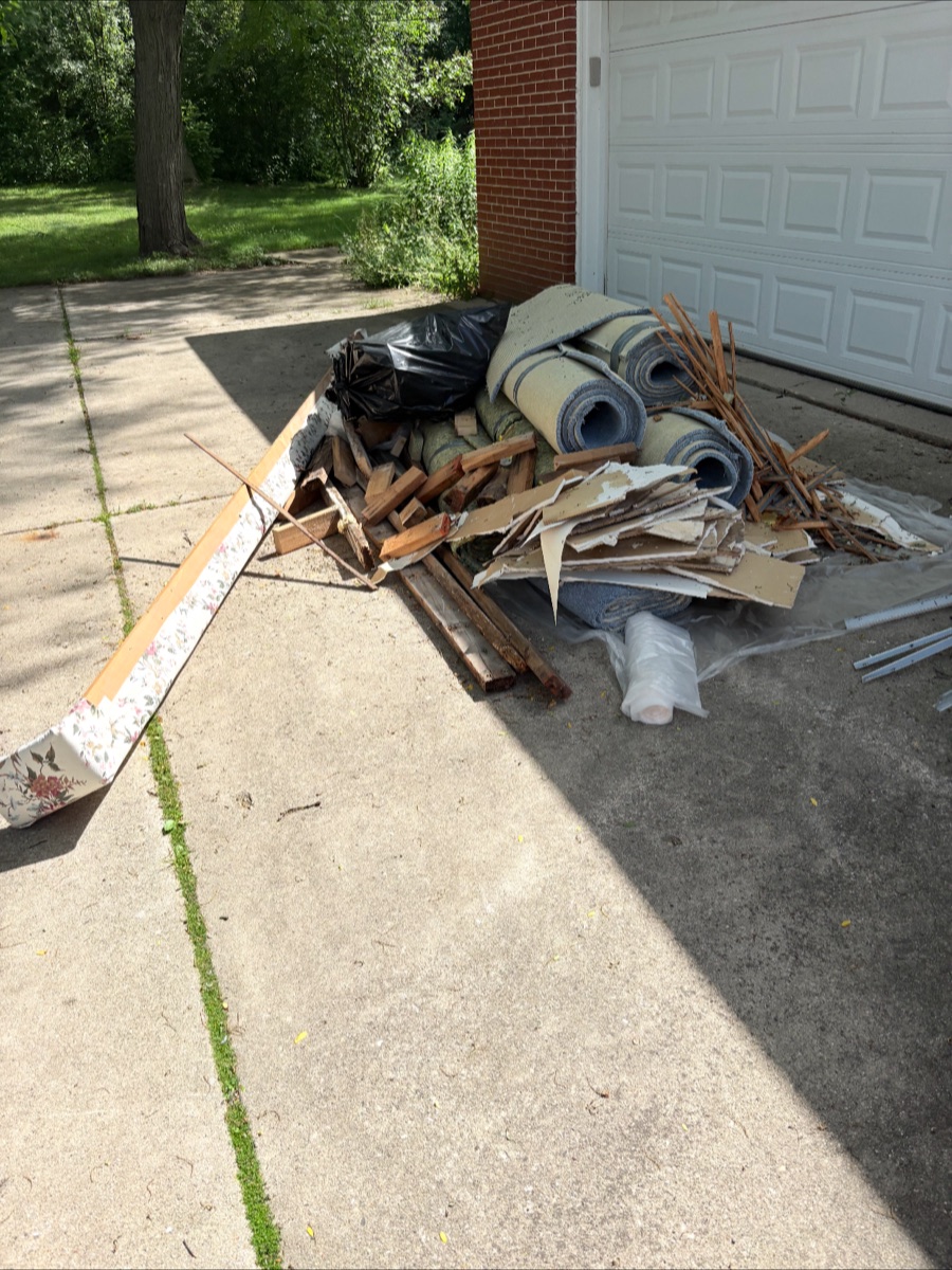 A driveway piled with old carpet, wood, and debris before TT's Junk Removal cleared it